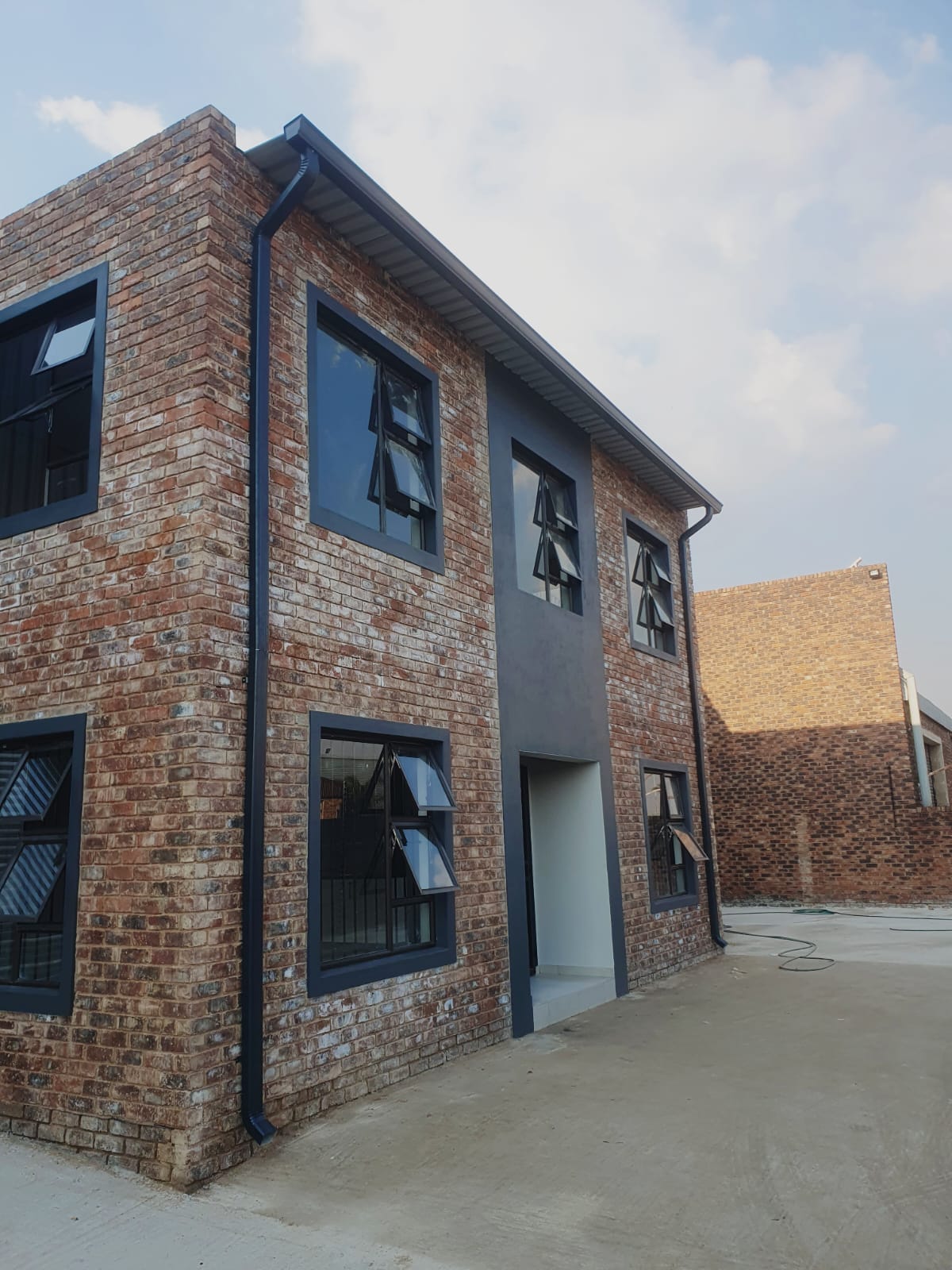 Black gutter and corner downpipe on a modern brick and grey render home